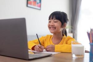 Asian girl student online learning class study online video call zoom teacher, Happy girl learn english language online with laptop at home.New normal.Covid-19 coronavirus.Social distancing.stay home photo