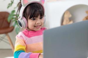 Smiling little Asian girl have a video call distant class with teacher using laptop, social distance during quarantine isolation during the Coronavirus photo
