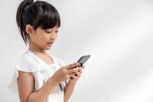 una niña pequeña se concentra en el teléfono, mira el teléfono inteligente, concepto de tecnología para niños, vista de perfil, aislada en fondo blanco, espacio de copia foto