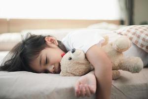 child little girl sleeps in the bed with a toy teddy bear photo