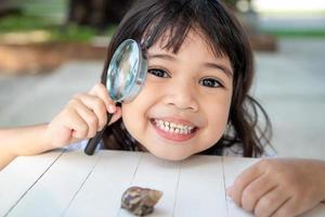 Happy kid girl exploring nature with a magnifying glass and a snail. He having fun in the garden. The concept of the kid is ready to go to school. photo