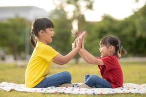 dos niñas sentadas en el césped del parque y jugando al juego de manos de piedra, papel y tijera foto