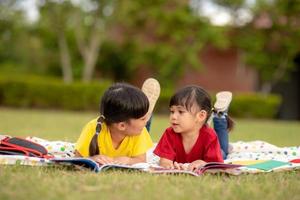 niña y hermana leyendo un libro juntos en el parque. adorables niños asiáticos disfrutando de estudiar juntos al aire libre. educación, concepto de inteligencia foto