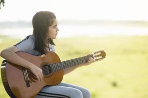 Lovely girl,playing guitar, singing ,music or happiness concept, sunset warm light tone effect. photo