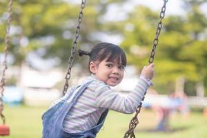 niña asiática feliz jugando al columpio al aire libre en el parque foto