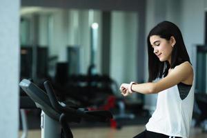 una niña mira el reloj inteligente después de entrenar en el gimnasio. concepto saludable. mujer después de la sesión de entrenamiento comprueba los resultados en el reloj.concepto deportivo para niños foto