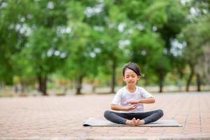 Little cute asian girl practicing yoga pose on a mat in park, Healthy and exercise concept photo