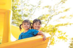 lindas niñas hermanos divirtiéndose en el patio de recreo al aire libre en un día soleado de verano. niños en tobogán de plástico. actividad divertida para niños. ocio deportivo activo para niños foto