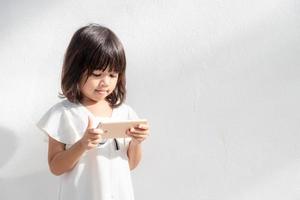 una niña pequeña se concentra en el teléfono, mira el teléfono inteligente, concepto de tecnología para niños, vista de perfil, aislada en fondo blanco, espacio de copia foto