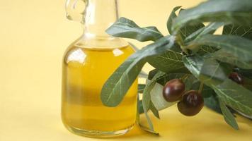 Olive branch and glass bottle of olive oil display on yellow table and background video