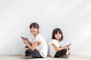 Sibling girls enjoy using smartphones on white background, the Concept of communication technology and people photo