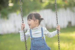 Happy little Asian girl playing swing outdoor in the park photo