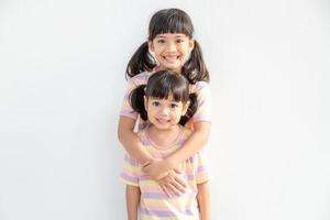 Cute happy Asian siblings hugging cuddling feeling love and connection, smiling kid girl sister embracing little girl sister on white background, 2 children good relationships photo