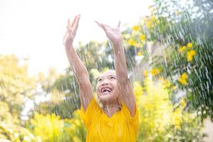 Happy Asian little child girl having fun to play with the rain in the sunlight photo