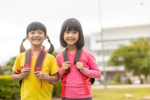 De vuelta a la escuela. dos lindas niñas asiáticas con mochila escolar sosteniendo un libro juntas en la escuela foto