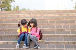 Two Little Girl reading a book together. Adorable Asian kids enjoying studying outdoors togther. Education, intelligence concept photo