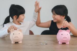 Two asian little girls having fun to put coin into Piggy Bank together,kid saving money for the future concept photo