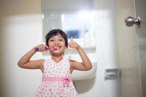 niñita linda limpiándose los dientes con cepillo de dientes en el baño foto