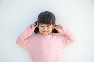 una linda niña asiática cubrió las orejas con los dedos y hizo un gesto de que no quería escuchar en un fondo blanco con un espacio de copia vacío
