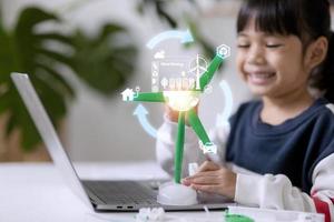 renewable energy, science, and technology concept - happy children with laptop computers, wind energy hologram,s and wind turbine models and icons. photo