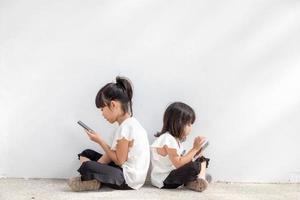 Sibling girls enjoy using smartphones on white background, the Concept of communication technology and people photo