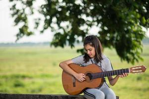 chica encantadora, tocando guitarra, cantando, música o concepto de felicidad, efecto de tono de luz cálido al atardecer. foto