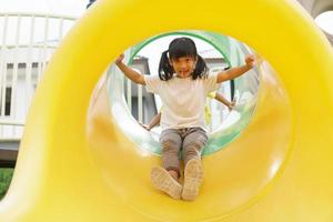 Child playing on outdoor playground. Kids play on school or kindergarten yard. Active kid on colorful slide and swing. Healthy summer activity for children. photo