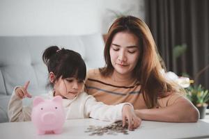 madre e hija poniendo monedas en la alcancía. presupuesto familiar y concepto de ahorro. concepto de cuenta de ahorro junior foto