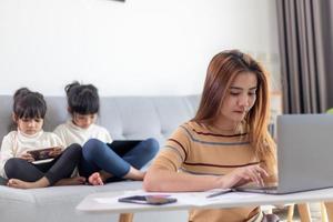 oficina en casa. trabajar desde casa frente a mamá con dos hijos trabajar en Internet en una computadora portátil en casa. cuarentena. coronavirus. foto