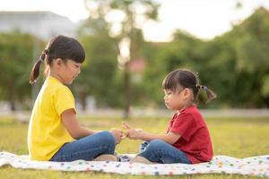 dos niñas sentadas en el césped del parque y jugando al juego de manos de piedra, papel y tijera foto