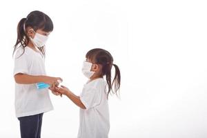 dos niñas pequeñas usan mascarilla durante el coronavirus y el brote de gripe. protección contra virus y enfermedades, desinfectante de manos.sobre fondo blanco foto