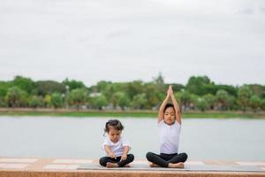 pequeña y linda niña asiática practicando pose de yoga en una alfombra en el parque, concepto saludable y de ejercicio foto