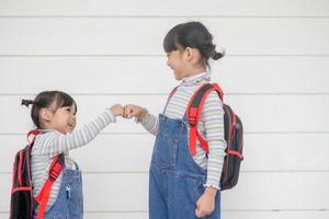 Back to school. Two cute Asian child girls with school bags holding a book together on white background photo