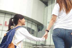 De vuelta a la escuela. madre asiática e hija alumna con mochila cogida de la mano y yendo juntas a la escuela. comienzo de las lecciones. primer día foto