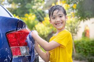 Cute asian child washing a car with hose on summer day photo