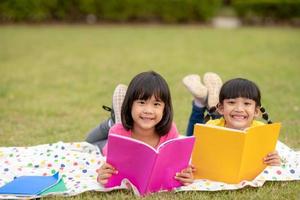 dos hermosas niñas leyendo libros en el jardín, sentadas en el césped. el concepto de educación y amistad. foto