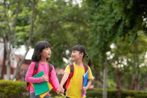 Back to school. Two cute asian child girls with school bag holding book and walk together in the school photo