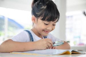 niña asiática leyendo los libros en el escritorio con una lupa foto