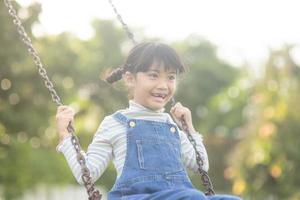 Happy little Asian girl playing swing outdoor in the park photo