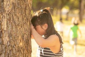 little girl is playing hide-and-seek hiding face in the park photo