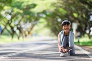 niño atando zapatos para correr. feliz y divertida niña asiática fitness mujer corriendo por la mañana. niño atlético corriendo en la naturaleza. estilo de vida saludable foto
