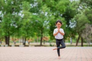 Little cute asian girl practicing yoga pose on a mat in park, Healthy and exercise concept photo