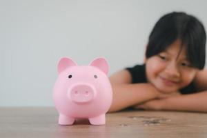 Cute asian child girl putting money into piggy bank to save money for the future photo