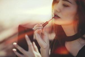mujer sexy haciendo mujer maquillada aplicando pintalabios al aire libre.color retro foto