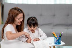 Beautiful Asian woman helping her daughter with homework at home. photo