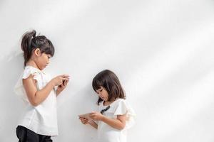 Sibling girls watching their smartphones on white background. Social concept about new technology people addiction photo