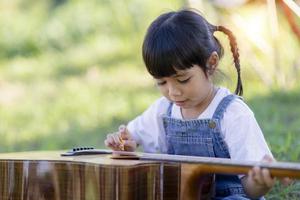 Happy Asian little child girl playing guitar or ukulele in the garden. Music,musician and guitarist concept. photo