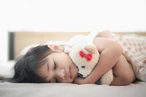 child little girl sleeps in the bed with a toy teddy bear photo