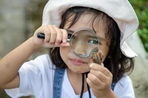 Happy kid girl exploring nature with a magnifying glass and a snail. He having fun in the garden. The concept of the kid is ready to go to school. photo