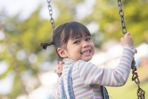 niña asiática feliz jugando al columpio al aire libre en el parque foto